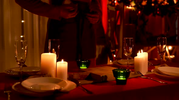 Woman Wipes Champagne Glasses While Standing Near Festive Table with Burning Candles and Utensils