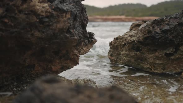 Wave crashes through rocks at the beach, slow motion, low gimbal zoom in