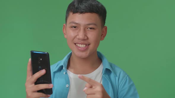 Smiling Young Asian Boy Use Phone And Pointing To Smart Phone Screen In The Green Screen Studio