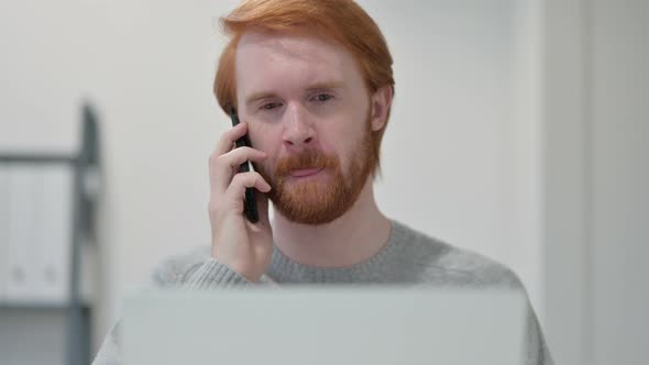 Portrait of Redhead Man with Laptop Talking on Smartphone 