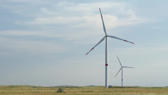 Motion the Blades of a Large Wind Turbine in a Field Against a Background of Orange Sunset on the