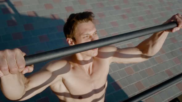 Young Athletic Man is Doing Pull Ups Exercises on Horizontal Bar During Intense Workout Outdoors