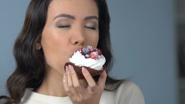 Asian Woman Enjoying Taste of Tasty Sweet Cupcake With Whipped Cream and Fruit