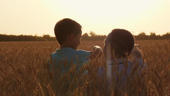 A Farmer and His Son in a Wheat Field at Sunset. Dad Shows the Child a Crop of Wheat.