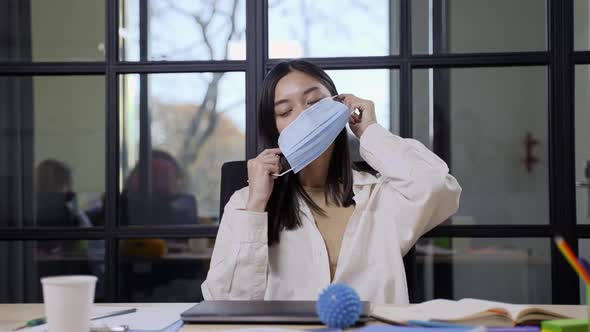 Young Asian Woman Putting on Face Mask in Office