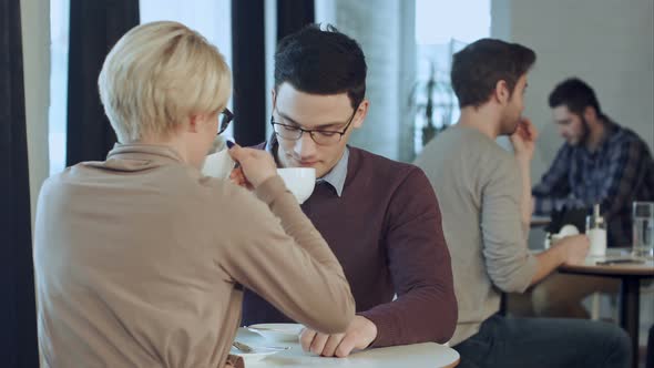 Young Couple Talking and Drinking Coffee Near the Window in Cafe