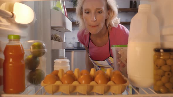 Mature Woman Taking Eggs From Fridge in Kitchen