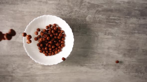 Full Plate of Chocolate Cornflakes in Form of Little Balls Fallen From Above in Slow Motion