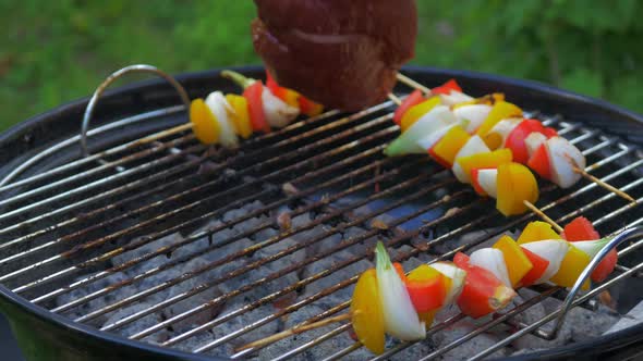 Flank steak mixed with vegetables on a skewer being grilled over hot coals. The steak is turned over