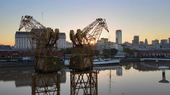 Slow aerial pan shot of old harbor cranes on quayside of Puerto Madero overlooking at downtown citys