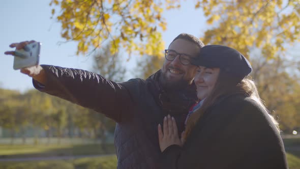 Cheerful Young Couple in Love Taking Selfie Using Smartphone at Autumn Park