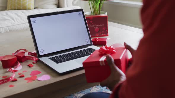 Midsection of biracial man holding present and having valentine's video call on laptop