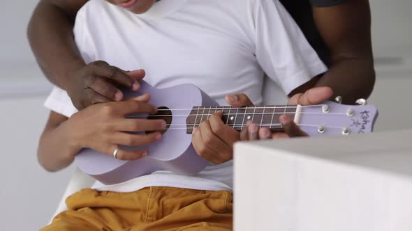 Closeup View of Young Dad and Son Playing Guitar While Sitting in Apartment Interior Spbi