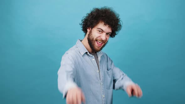 Young Man with Kinky Hair Points Fingers to Camera Smiling