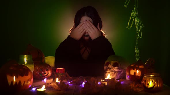 A Witch Closes Her Eyes Then Ears and Mouth Sitting Among Halloween Decorations