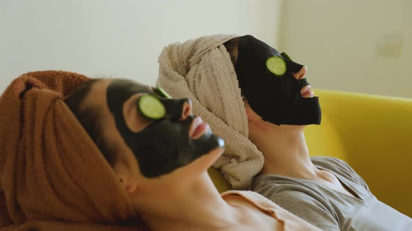 Two Young Woman Lying with Cosmetic Masks on Their Faces and Cucumber Slices on Their Eyes