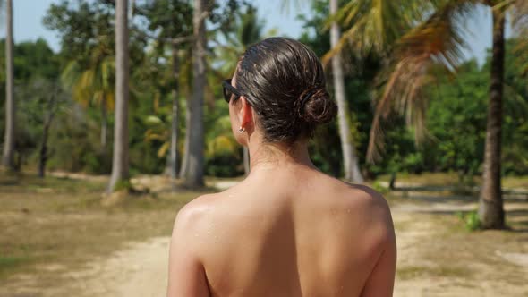 Girl Walks Through Grove and Turns Back Against Palm Trees