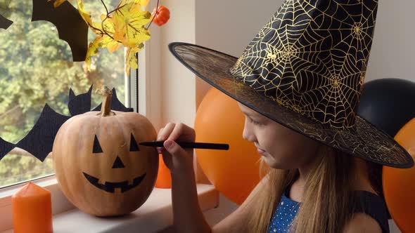 Little Girl in Witch Costume Drawing Scary and Funny Jack O Lantern Face on Pumpkin with Black