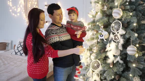 Parents with Daughter Decorate Illuminated Christmas Tree