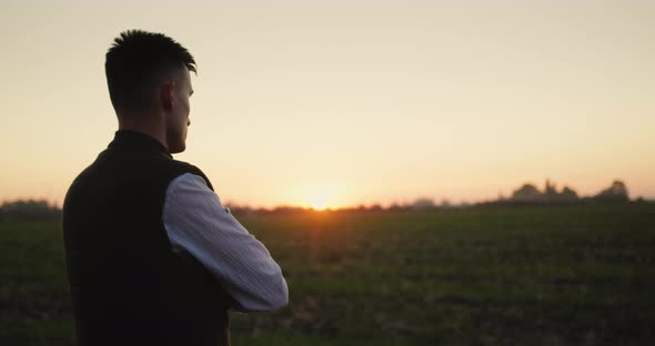 A Man Farmer Looks Into the Distance at His Field Stands Alone at Sunset