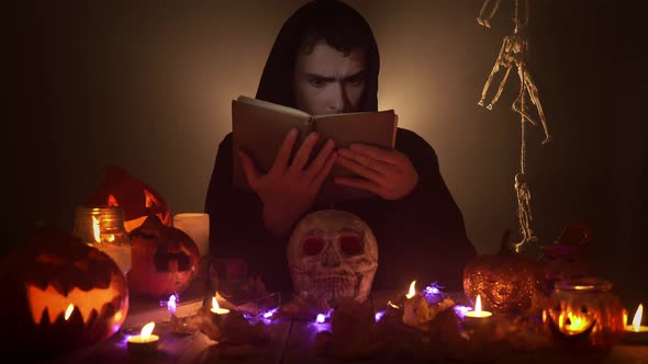 Portrait of Man in the Image of Wizard Reading Voodoo Book Among Candles and Jack O'lanterns