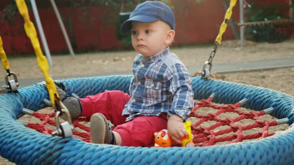 Toddler Boy Swings on a Round Swing on the Playground