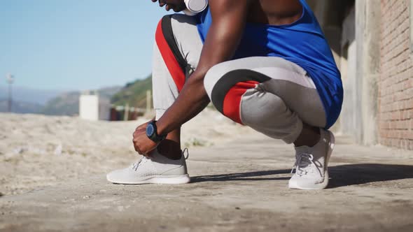 Midsection of african american man tying shoelaces during exercise outdoors on beach