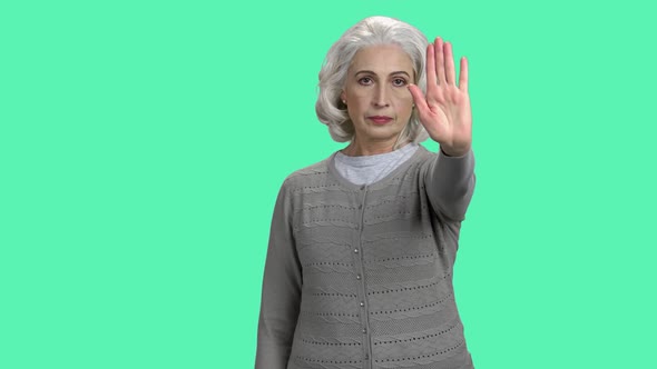 Mature Woman Showing Stop Gesture on Turquoise Background