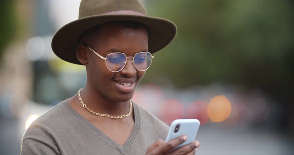 Bokeh Shot of Happy African Young Man Using Mobile Phone Outdoors