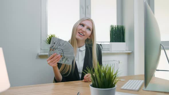 Smiling Business Woman Holding Wad of Cash. Beautiful Happy Blond Female Sitting in Office at