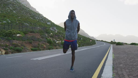 African american man wearing a hoodie performing stretching exercise on the road