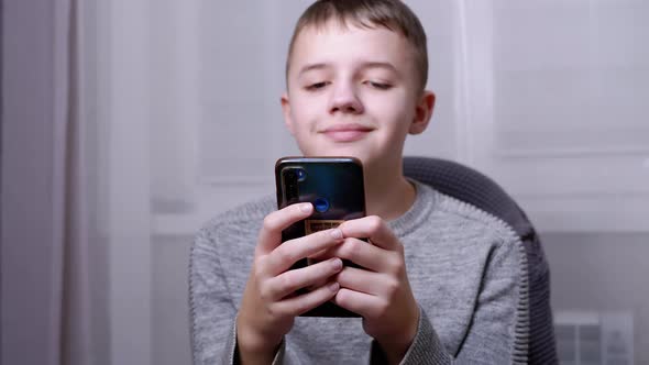 Smiling Child Sits in a Chair Holds a Smartphone in Hands Reads SMS on Screen