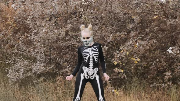 A girl with a scary make-up in a skeleton costume, a mask with rhinestones in a gloomy autumn forest