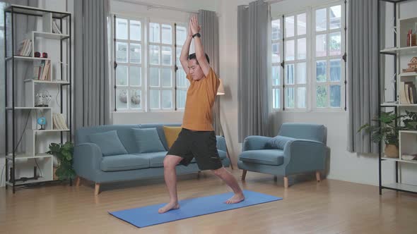 Asian Man Doing Yoga In Warrior I Pose On Mat  At Home