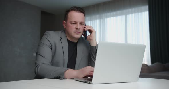 Businessman Working On Laptop And Talking On Mobile Indoors