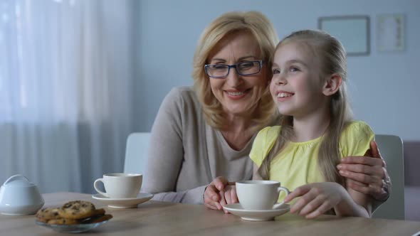 Loving Grandma Drinking Tea With Cute Granddaughter, Holding Her Hand, Family