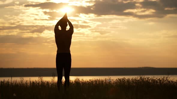 Silhouette of Young Sportive Man Practicing Yoga at Sunset