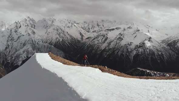 Aerial View Young Man in Sunglasses with a Backpack Goes Down the Mountain on the Crest on the