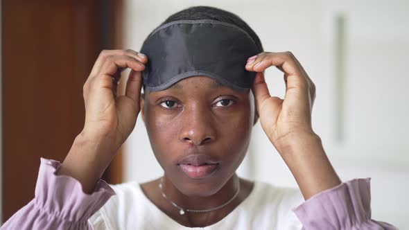 Closeup Portrait of Young African American Woman Taking Off Sleeping Eye Mask Looking at Camera