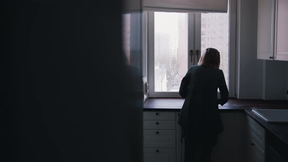 Depressed Lonely Elderly Woman Leaning on the Kitchen Cupboard and Looking Through the Window