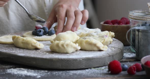 Raw pierogi with berry on a wooden board with women  hands