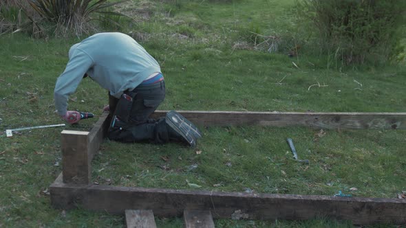 Young man building raised garden bed with planks