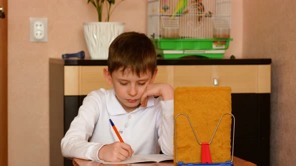 Caucasian boy of primary school age, sitting at the table, writes in a notebook, does his homework