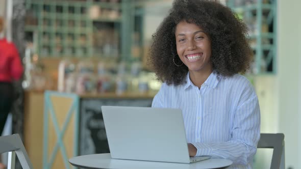 Young African Woman with Laptop Smiling at Camera in Cafe 