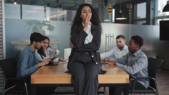 Worried Young Hispanic Girl in Business Suit Sitting on Table in Conference Room Busy Multicultural