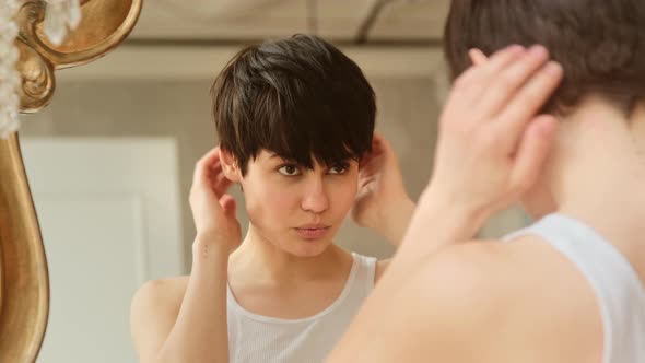 Young woman fixing short hair looking in mirror getting ready at home. Haircare