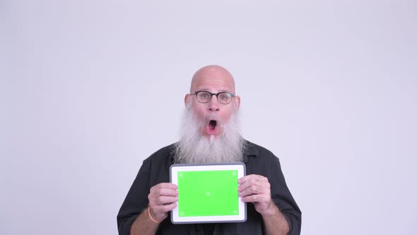 Mature Bald Bearded Man Looking Shocked While Showing Digital Tablet