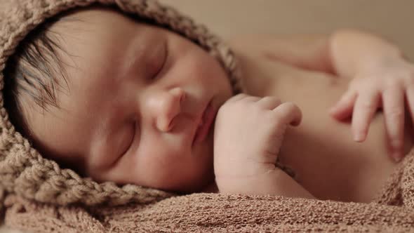 Newborn baby sleeping peacefully with checkered cloth on brown background