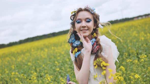 A Young Girl Poses in a Rapeseed Field with a Beautiful Hairdo of Flowers and Butterflies