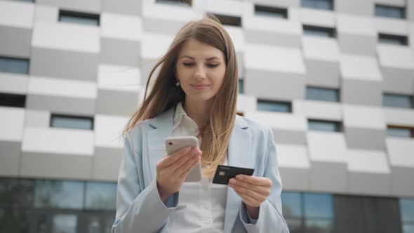 Smiling Young Woman Customer Holding Credit Card and Smartphone